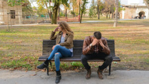 An unhappy couple sitting on a bench at a park.