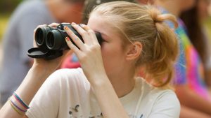 A girl in a white T-shirt looks through binoculars