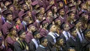 Graduates in maroon robes stand at JQH Arena