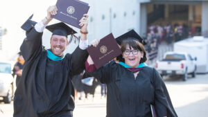 A male and female graduate show hold up their degrees.