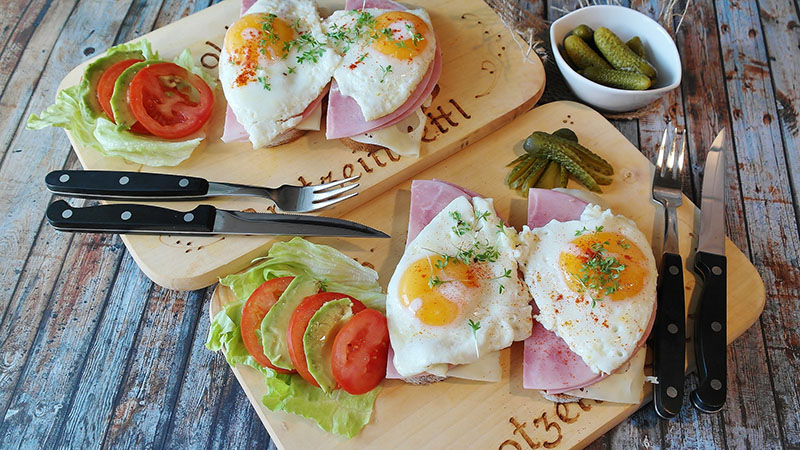 Two platters of eggs, ham and cheese sandwiches with a side of lettuce, tomatoes and dill pickles.