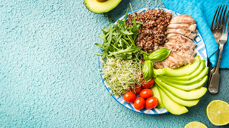 A plate with ingredients of balanced healthy food - quinoa, tomatoes, chicken, avocado and mixed greens.