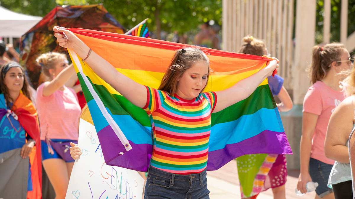 Person holding rainbow flag behind their head