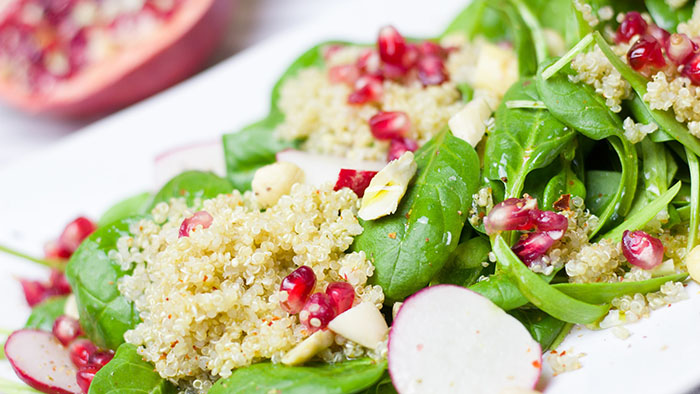 A plate of spinach salad with pomegranate and couscous.