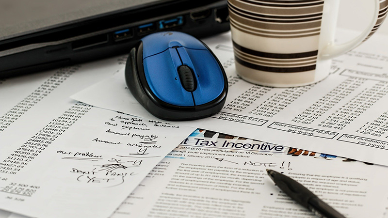 Tax documents along with a pen, mouse, coffee mug and laptop.