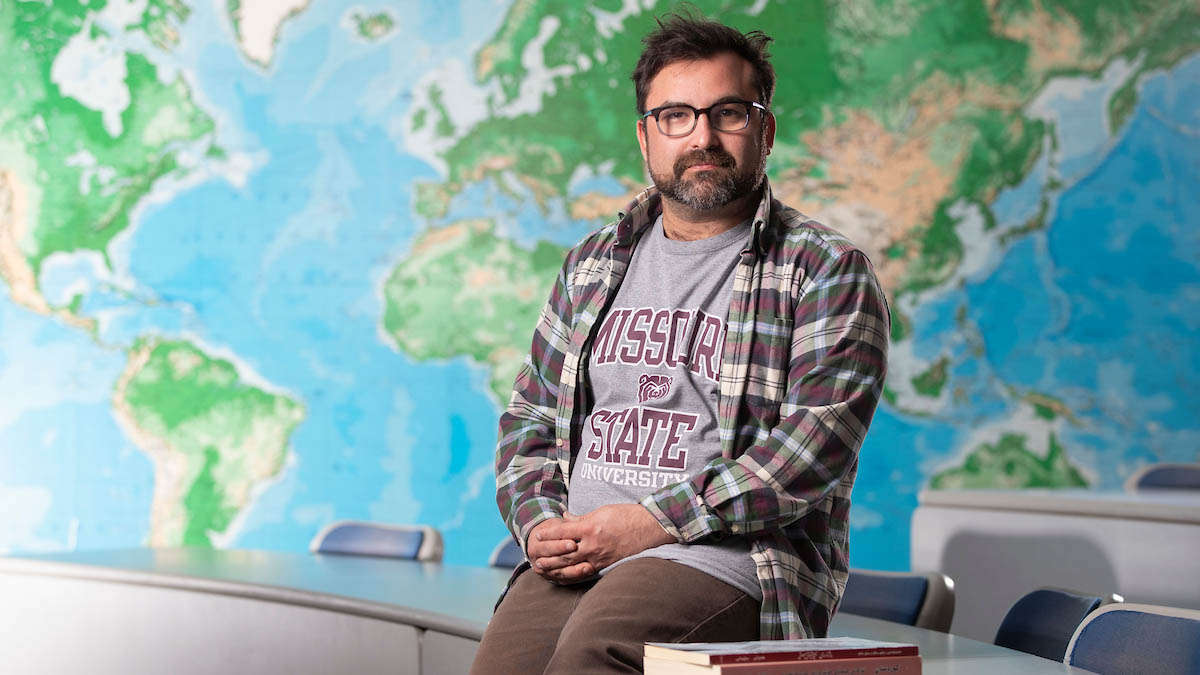 Man sits on desk in front of world map