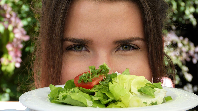A lady holding up a plate of salad.