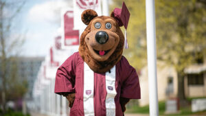Boomer the Bear in graduation regalia on the Missouri State University campus.