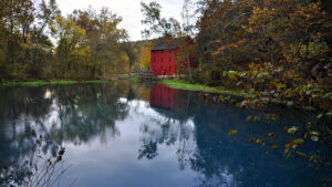 Ozarks scenery: a red building by a lake surrounded with trees.