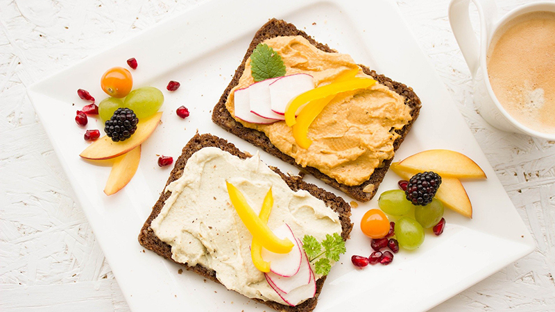 A healthy breakfast of hummus on whole wheat bread with assorted fruits.