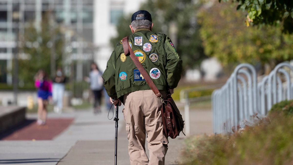 Man wearing jacket with military insignia walks toward Strong Hall.