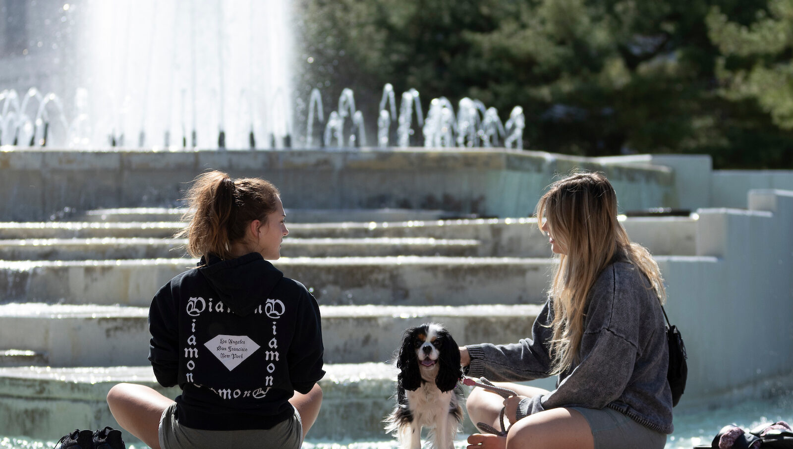 Two girls and a small dog sitting on the ledge of the fountain.