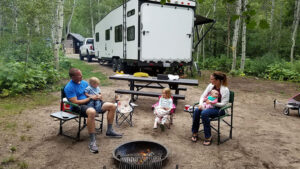 A family with young kids sitting around a campfire.