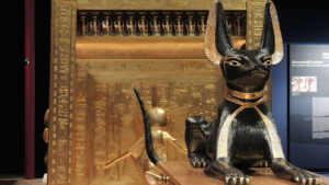 A large black and gold cat sculpture in front of Egyptian motifs in gold.