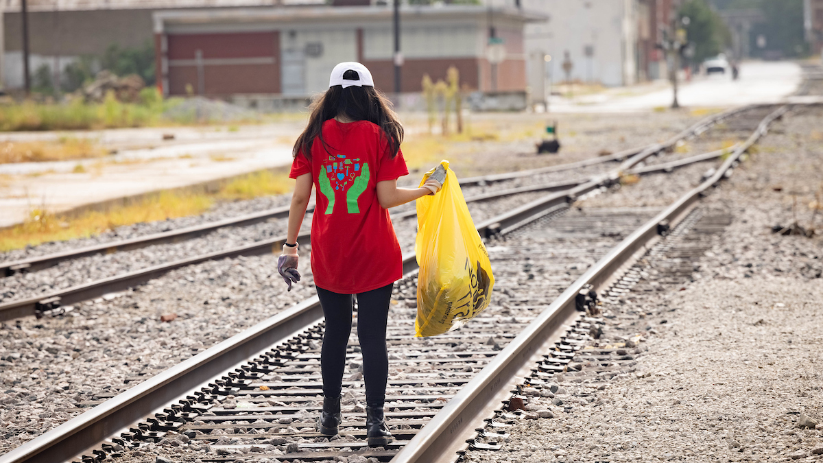 Female student walks on railroad track searching for trash in downtown Springfield.