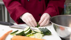 A chef preps vegetables in the kitchen with gloved hands.
