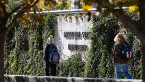 Two students walking past the Missouri State University wall on campus.