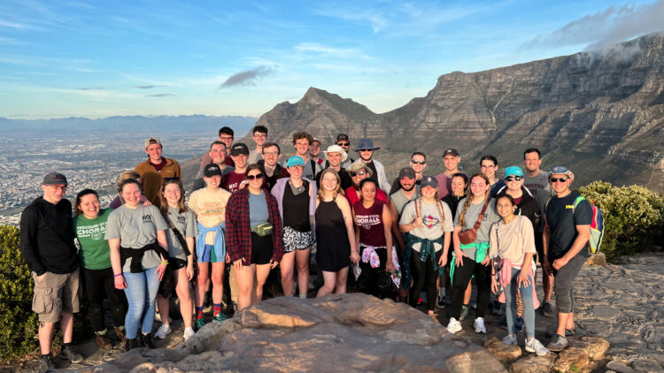 Chorale poses in front of mountain overlooking sea.