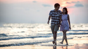 An Asian couple walking on the beach.