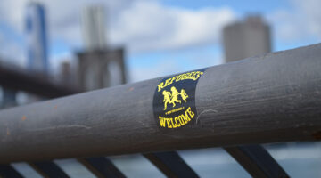 A refugees welcome sticker on a wooden rail.