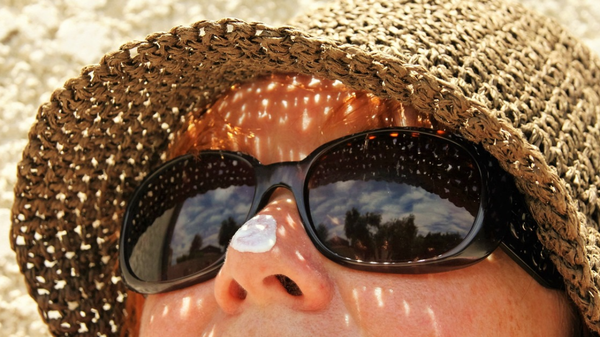 Woman wears hat and sunblock outside.