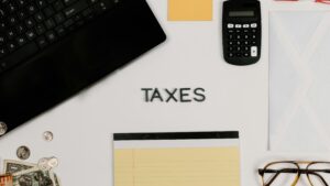 The word "TAXES" on a table surrounded by a laptop, notepad and calculator.