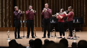 Five students blowing their trumpets on stage.