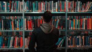 A person wearing a black and grey hoodie looking at a bookshelf.