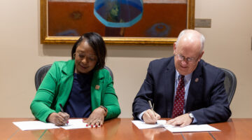 A woman and man sit at a table signing an agreement.