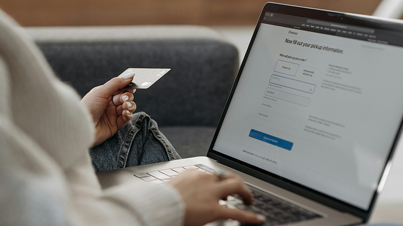 A person with a credit card in her left hand and typing on a laptop with the right hand.