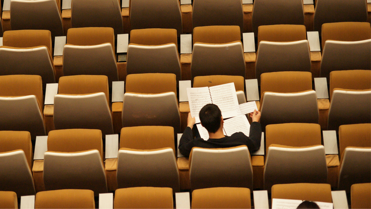 A person reading a book in an auditorium filled with empty brown seats.