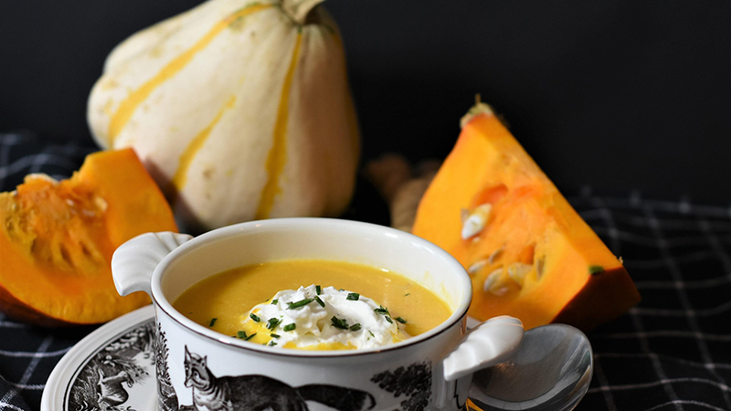 A bowl of pumpkin soup with some pumpkin around it.