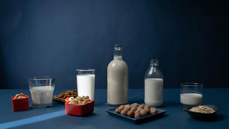 Different types of plant-based milk in glass cups and bottles.